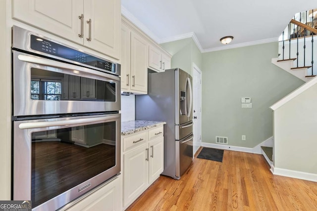 kitchen featuring light hardwood / wood-style flooring, ornamental molding, light stone counters, white cabinetry, and stainless steel appliances