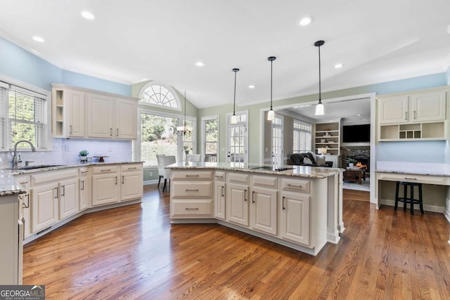 kitchen with pendant lighting, sink, vaulted ceiling, a fireplace, and a kitchen island