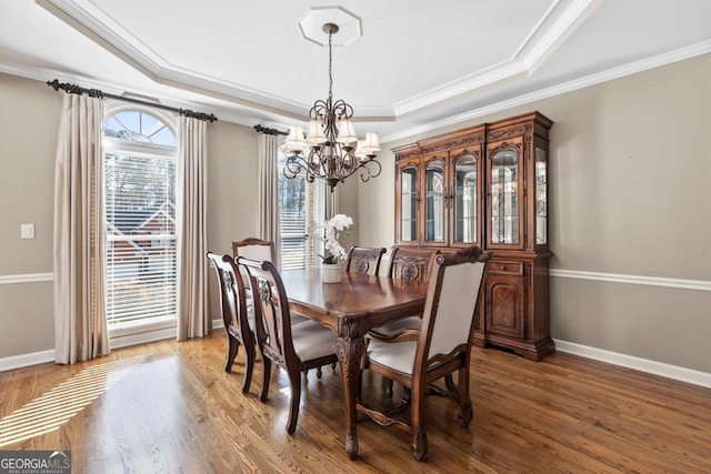 dining area featuring a chandelier, wood-type flooring, a tray ceiling, and ornamental molding