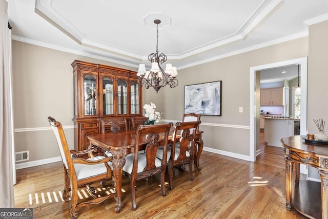 dining area featuring a notable chandelier, a raised ceiling, light wood-type flooring, and crown molding