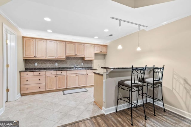 kitchen with a kitchen breakfast bar, backsplash, pendant lighting, light brown cabinetry, and ornamental molding