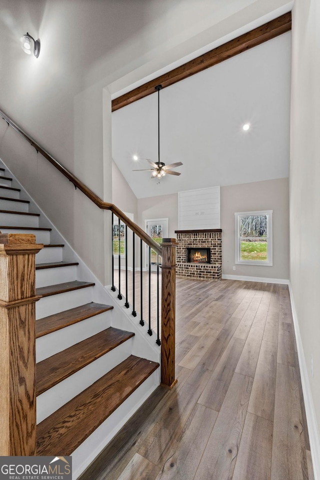 stairs featuring beam ceiling, wood-type flooring, a brick fireplace, high vaulted ceiling, and baseboards