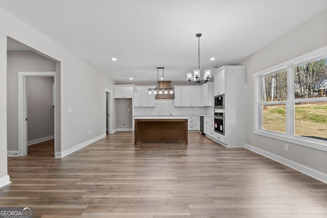 kitchen with light wood finished floors, white cabinets, decorative backsplash, an inviting chandelier, and stainless steel appliances