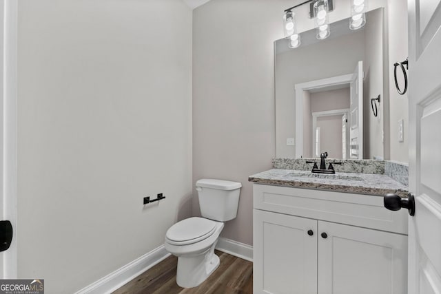 half bathroom with toilet, baseboards, wood finished floors, and vanity