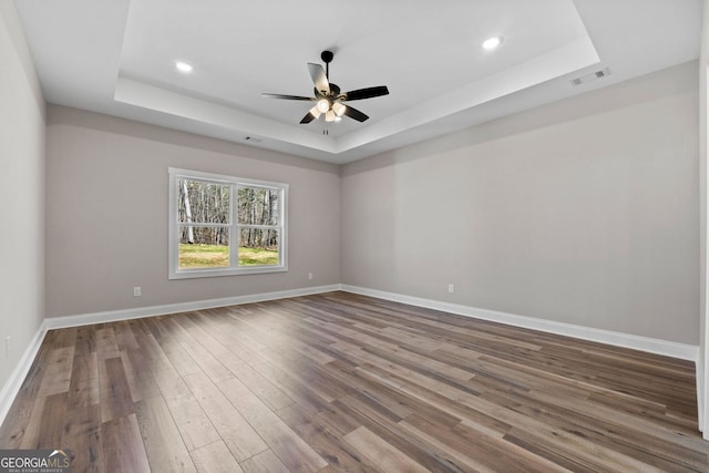 spare room featuring baseboards, visible vents, a raised ceiling, and wood finished floors