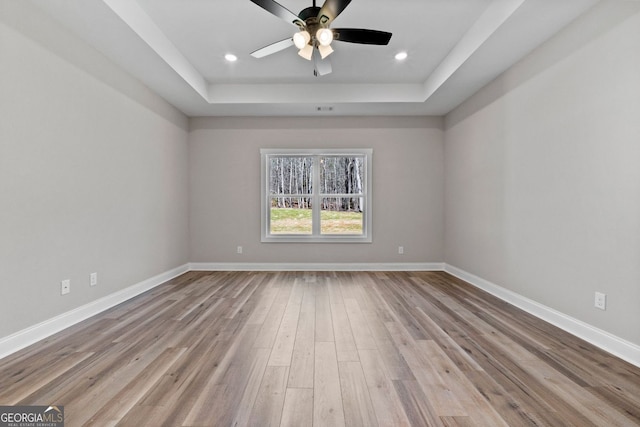 unfurnished room with a tray ceiling, wood finished floors, and baseboards