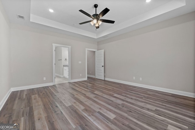 unfurnished bedroom featuring wood finished floors, ensuite bath, a raised ceiling, and baseboards