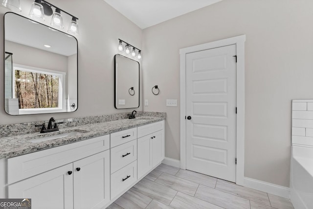 bathroom featuring double vanity, a tub, baseboards, and a sink