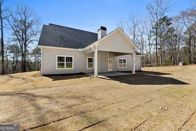 rear view of property featuring a shingled roof, a chimney, and a patio