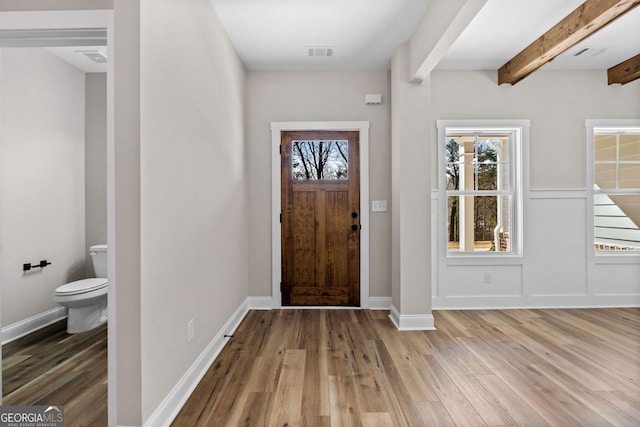 foyer with beam ceiling, visible vents, baseboards, and wood finished floors