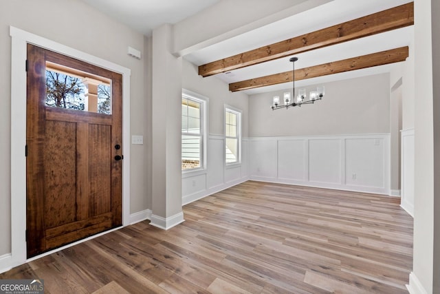 entrance foyer featuring a chandelier, beamed ceiling, light wood-style flooring, and a healthy amount of sunlight