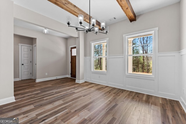 unfurnished dining area featuring visible vents, beamed ceiling, wood finished floors, a chandelier, and a decorative wall