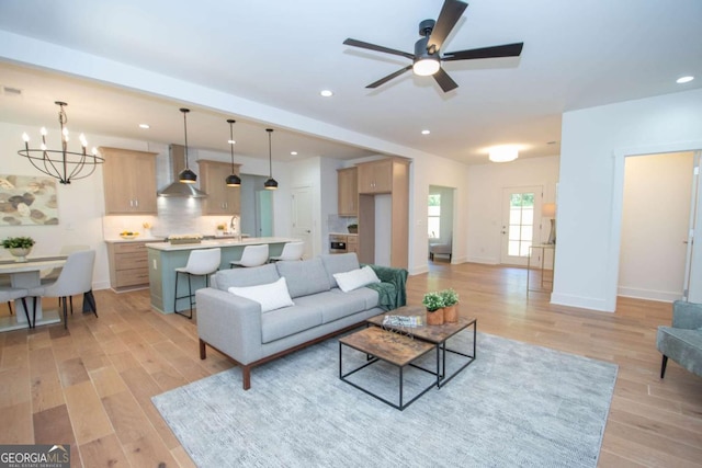 living room featuring sink, ceiling fan with notable chandelier, and light wood-type flooring