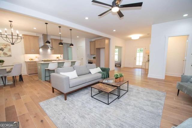 living room with ceiling fan with notable chandelier and light hardwood / wood-style flooring