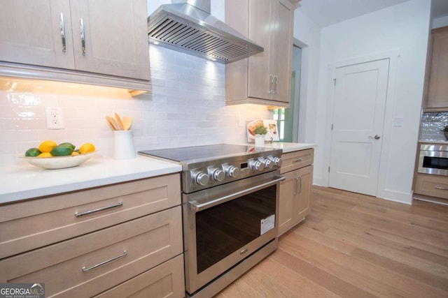 kitchen featuring stainless steel appliances, wall chimney range hood, light hardwood / wood-style floors, decorative backsplash, and light brown cabinetry