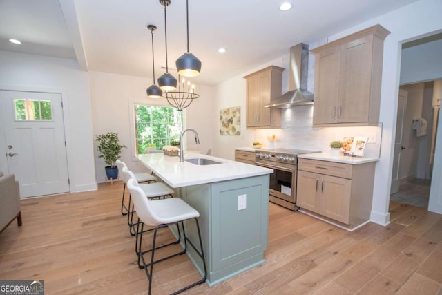 kitchen featuring a kitchen island with sink, wall chimney range hood, sink, electric stove, and decorative light fixtures