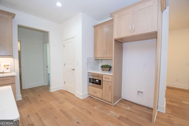 kitchen with built in microwave, backsplash, light brown cabinetry, and light hardwood / wood-style flooring