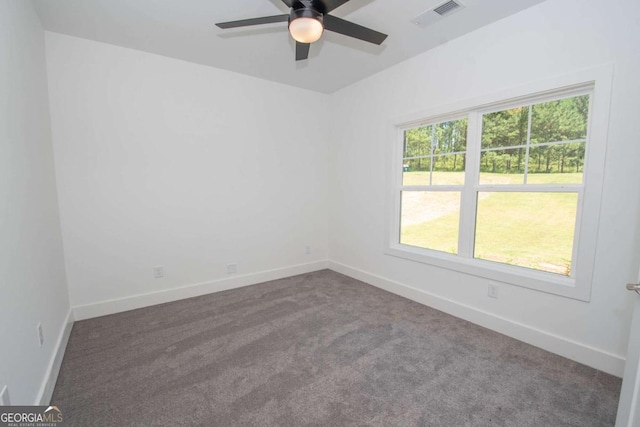 spare room with dark colored carpet, a wealth of natural light, and ceiling fan