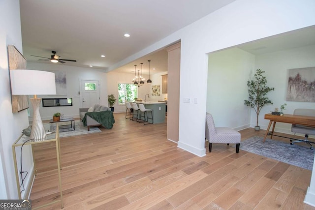 living room with ceiling fan with notable chandelier, light hardwood / wood-style flooring, and sink