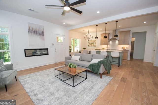 living room with ceiling fan with notable chandelier and light hardwood / wood-style floors