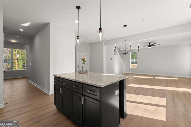 kitchen featuring pendant lighting, a healthy amount of sunlight, ceiling fan with notable chandelier, a kitchen island, and light stone counters