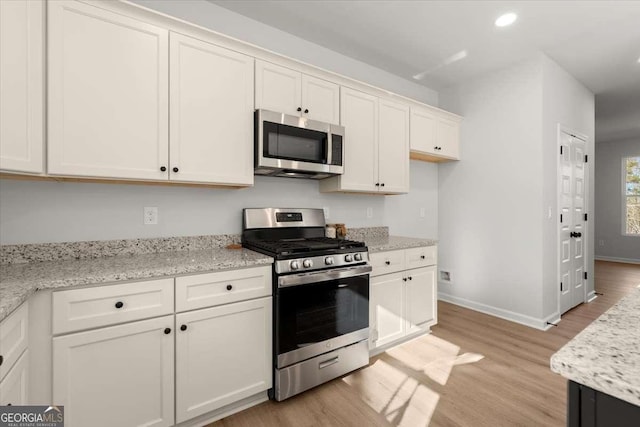 kitchen with white cabinetry, light hardwood / wood-style floors, light stone counters, and appliances with stainless steel finishes