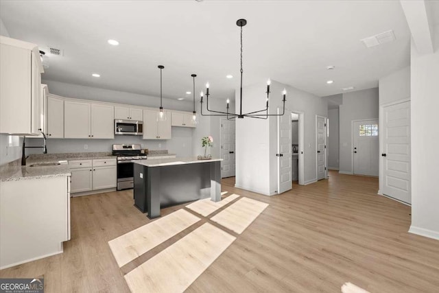 kitchen featuring white cabinets, sink, hanging light fixtures, a kitchen island, and stainless steel appliances