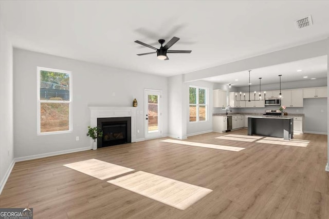 unfurnished living room featuring light wood-type flooring, ceiling fan, and a healthy amount of sunlight