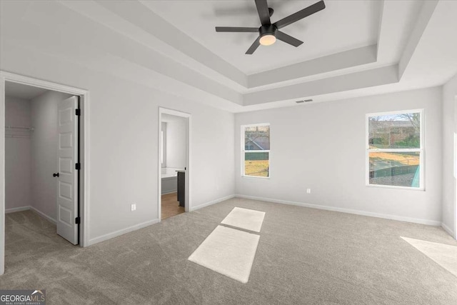 unfurnished bedroom with connected bathroom, a tray ceiling, a spacious closet, and light colored carpet