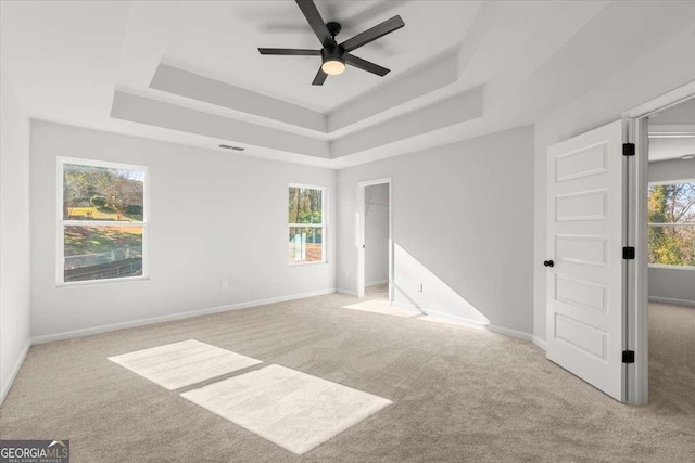 spare room with light carpet, a tray ceiling, and ceiling fan