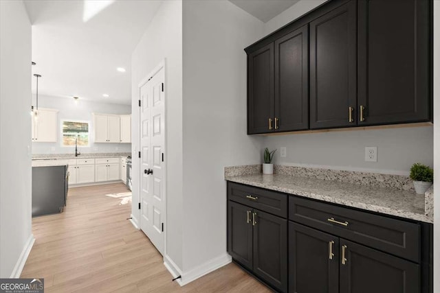 kitchen featuring light hardwood / wood-style floors, light stone countertops, white cabinetry, and hanging light fixtures