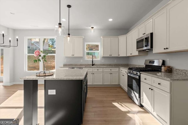 kitchen with light stone countertops, white cabinetry, a center island, stainless steel appliances, and light wood-type flooring