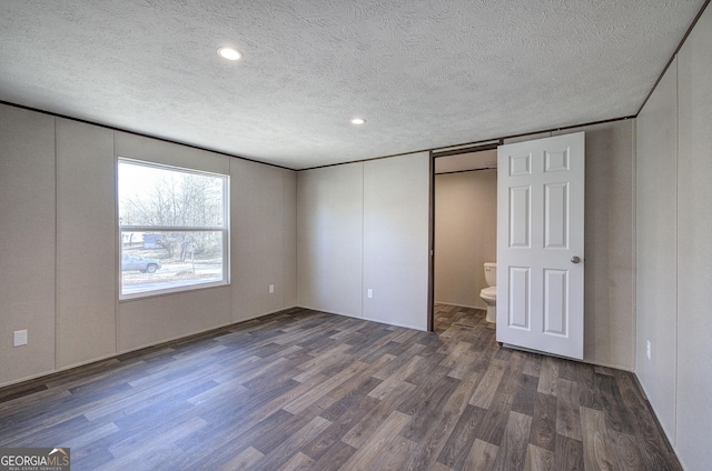 unfurnished bedroom featuring a textured ceiling, ensuite bathroom, and dark wood-type flooring