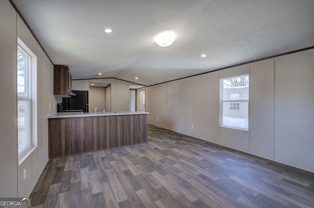 kitchen with kitchen peninsula, dark hardwood / wood-style flooring, black fridge, a textured ceiling, and lofted ceiling