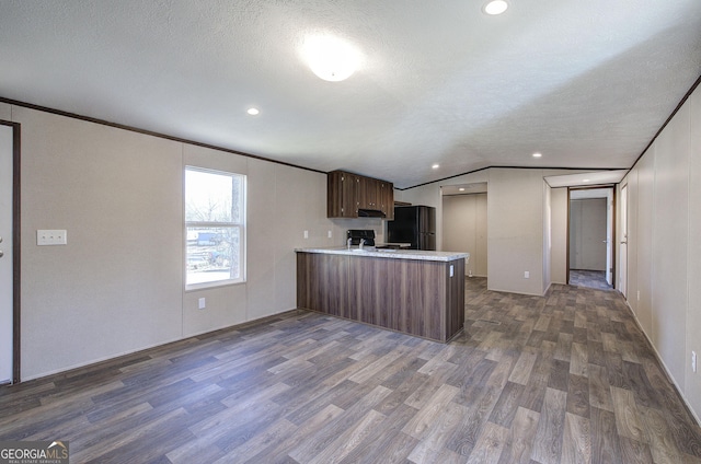 kitchen with dark wood-type flooring, kitchen peninsula, vaulted ceiling, a textured ceiling, and black appliances