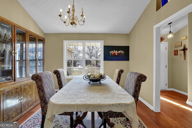 dining room with hardwood / wood-style floors, lofted ceiling, and an inviting chandelier