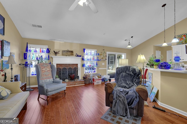 living room with vaulted ceiling, hardwood / wood-style flooring, a brick fireplace, and ceiling fan