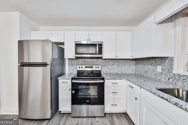 kitchen with light stone counters, white cabinets, stainless steel appliances, and light hardwood / wood-style floors