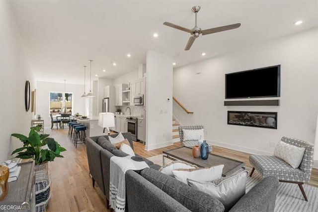 living room featuring ceiling fan, sink, and light hardwood / wood-style floors