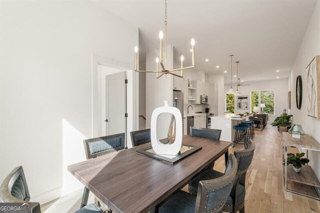 dining area featuring ceiling fan with notable chandelier, sink, and light hardwood / wood-style flooring