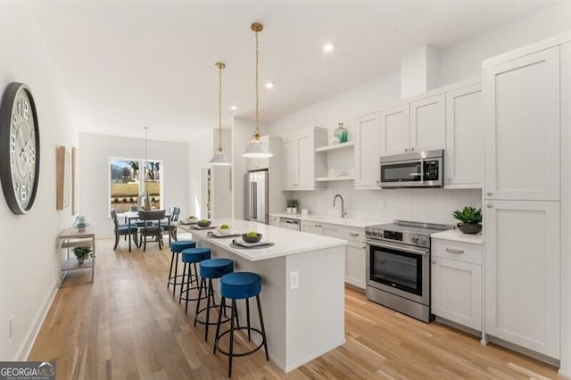 kitchen featuring appliances with stainless steel finishes, white cabinets, a center island, hanging light fixtures, and a breakfast bar area