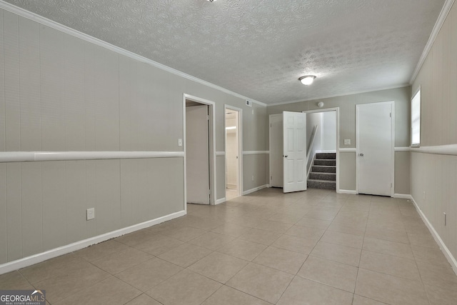 unfurnished room featuring wooden walls, light tile patterned flooring, a textured ceiling, and ornamental molding