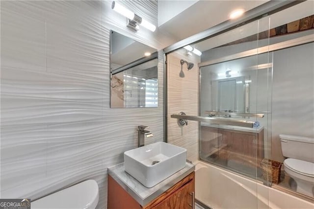 full bathroom featuring vanity, toilet, bath / shower combo with glass door, and tile walls