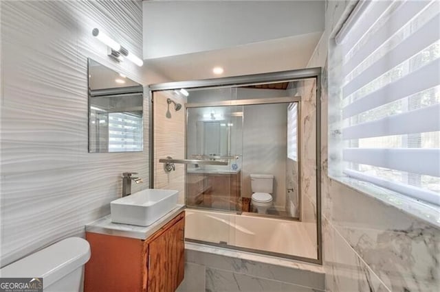 full bathroom with vanity, toilet, bath / shower combo with glass door, and tile walls