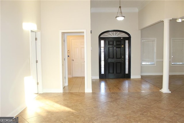 tiled entryway featuring decorative columns, a high ceiling, and ornamental molding