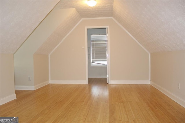 bonus room with a textured ceiling, lofted ceiling, and light hardwood / wood-style flooring