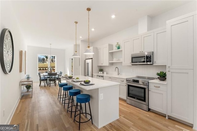 kitchen featuring a center island, white cabinets, a kitchen breakfast bar, appliances with stainless steel finishes, and decorative light fixtures