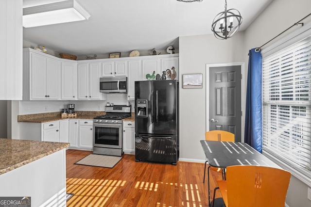 kitchen with appliances with stainless steel finishes, decorative light fixtures, an inviting chandelier, stone countertops, and white cabinets