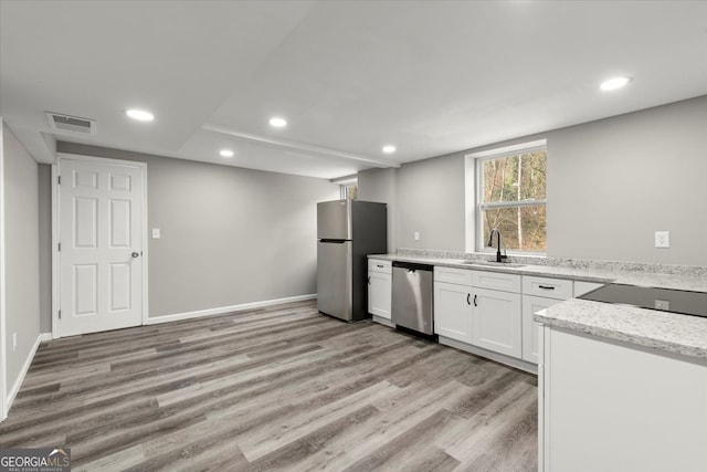 kitchen featuring sink, light stone countertops, appliances with stainless steel finishes, light hardwood / wood-style floors, and white cabinetry