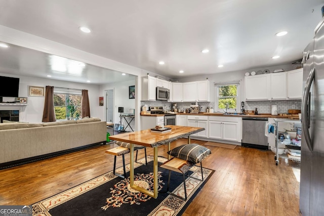 kitchen featuring sink, backsplash, appliances with stainless steel finishes, white cabinets, and light wood-type flooring